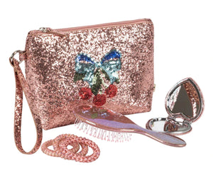 The Konges Slojd Get Ready With Me Set includes a glittery pink cosmetic clutch with sequin bow and cherries, a pink hair brush, coiled hair ties, and a heart-shaped hand mirror for quick touch-ups anywhere.