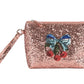 The Get Ready With Me Set by Konges Slojd is a pink glittery wristlet pouch with a zipper and a decorative patch of a blue bow and red cherries—ideal as a cute toiletry bag for your essentials.