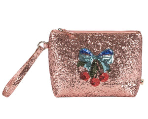 The Get Ready With Me Set by Konges Slojd is a pink glittery wristlet pouch with a zipper and a decorative patch of a blue bow and red cherries—ideal as a cute toiletry bag for your essentials.