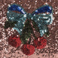 The Get Ready With Me Set by Konges Slojd features a sequin patch of a blue-green bow with red cherries on a pink background—perfect for adding vibrant flair to your toiletry bag or hand mirror.