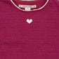 Close-up of the Konges Slojd Baby Girls' and Girls' Roli Blouse, a magenta knit top with lurex sparkle, featuring a small white heart near the neckline and delicate white lace trim on the collar.