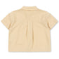 The Konges Slojd Baby Boys’ and Boys’ Franzen Short Sleeve Linen Shirt is pictured from the back, showcasing a beige linen-blend design with short sleeves, a collared neckline, central pleat, and a small loop beneath the collar. This breathable shirt delivers comfort and effortless style for everyday wear.