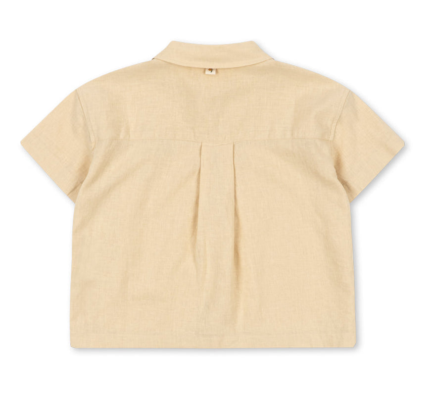 The Konges Slojd Baby Boys’ and Boys’ Franzen Short Sleeve Linen Shirt is pictured from the back, showcasing a beige linen-blend design with short sleeves, a collared neckline, central pleat, and a small loop beneath the collar. This breathable shirt delivers comfort and effortless style for everyday wear.