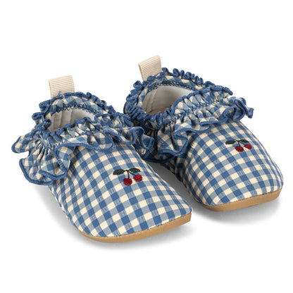The Fresia Frill Swim Shoes by Konges Slojd feature a blue and white gingham pattern with ruffled trim and a delicate cherry embroidery on the front. Crafted from quick-drying fabric offering UPF 40+ protection, these baby swim shoes are shown on a white background.