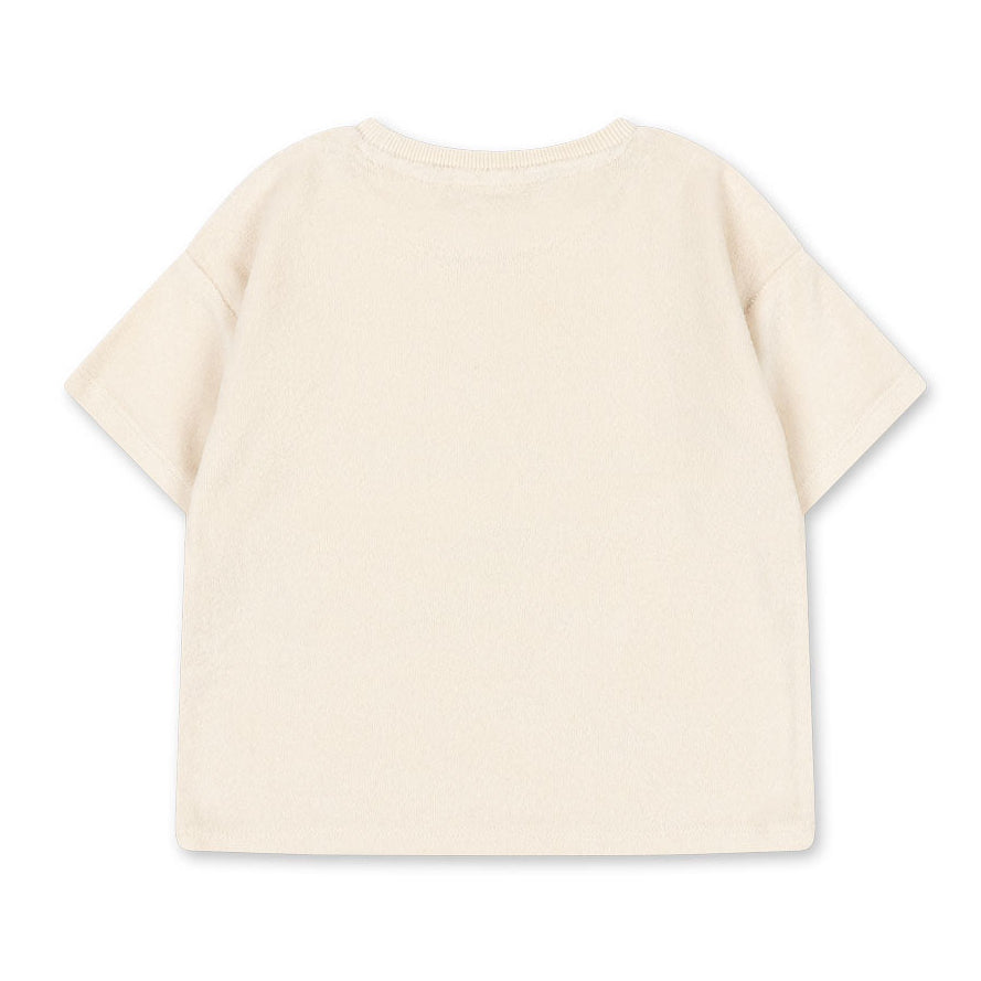 The Konges Slojd Baby Boys’ Itty Tee, a short-sleeved off-white t-shirt crafted from organic cotton terry, is displayed laid flat with the back facing up against a white background.