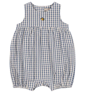 The Baby Kim Romper by Konges Slojd features a sleeveless design in a blue and white checkered seersucker fabric, a gathered waist, delicate elastic cuffs for extra comfort, snap buttons at the bottom, and is adorned with a small embroidered yellow flower.