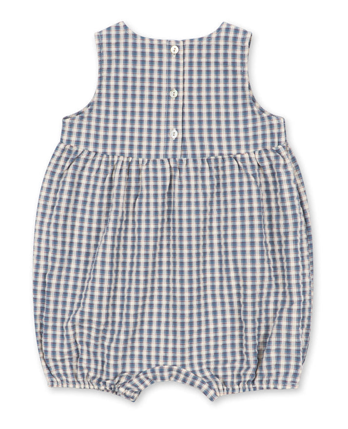 The Konges Slojd Baby Kim Romper is a sleeveless seersucker romper for babies, showcasing a charming blue and white plaid pattern, gathered waist, elasticized leg openings, and three snap buttons on the back.