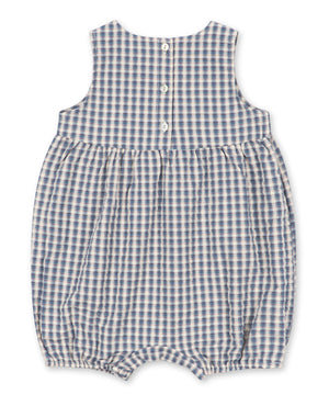 The Konges Slojd Baby Kim Romper is a sleeveless seersucker romper for babies, showcasing a charming blue and white plaid pattern, gathered waist, elasticized leg openings, and three snap buttons on the back.