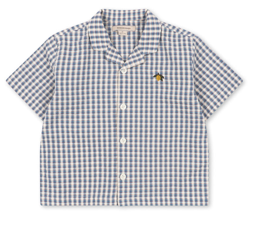The Konges Slojd Baby Boys’ and Boys’ Kim Short Sleeve Shirt features a charming blue and white check seersucker pattern, crafted from soft organic cotton, and is finished with a small embroidered bee on the left chest.