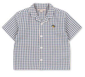 The Konges Slojd Baby Boys’ and Boys’ Kim Short Sleeve Shirt features a charming blue and white check seersucker pattern, crafted from soft organic cotton, and is finished with a small embroidered bee on the left chest.