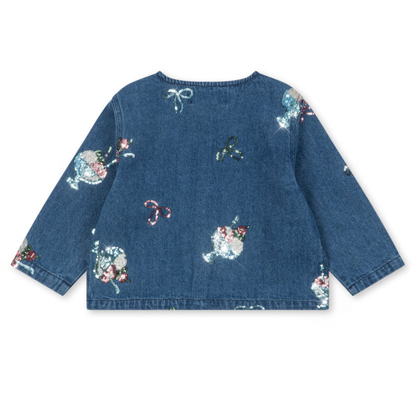 The Girls’ Magot Sequin Denim Jacket by Konges Slojd is a blue long-sleeve denim shirt jacket adorned with multicolored sequin appliqué bows, round shapes, and playful embroidered motifs scattered across the fabric.