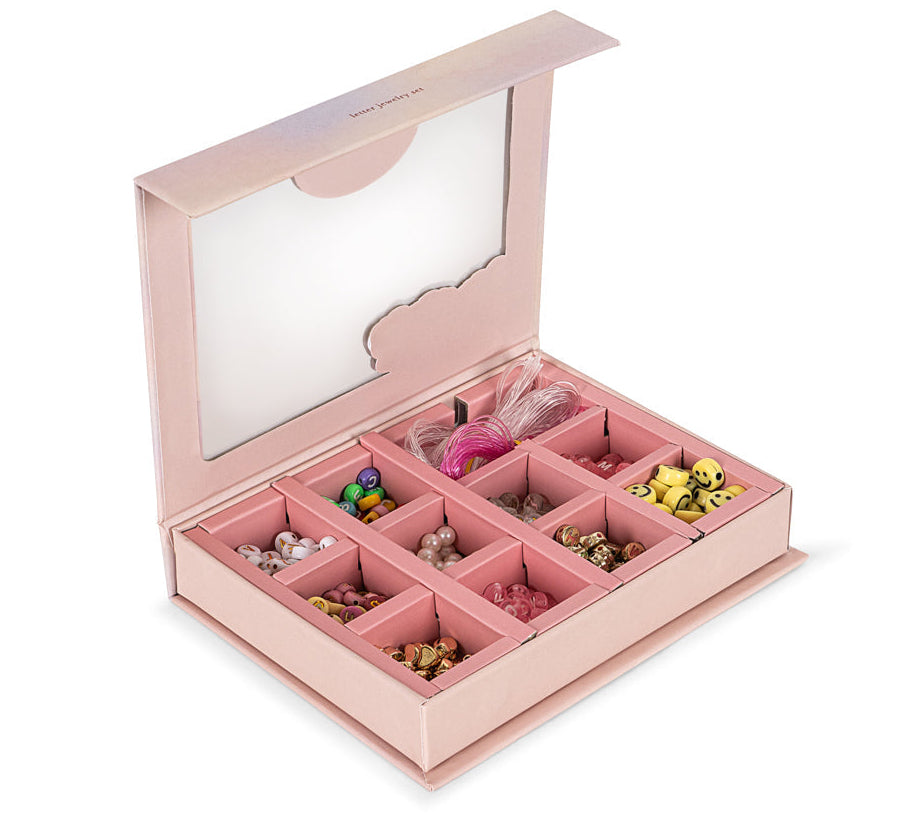The ABC Jewelery Set by Konges Slojd is a pink bead box with a clear lid, featuring 9 compartments of colorful trinkets and letter pearls for jewellery making.