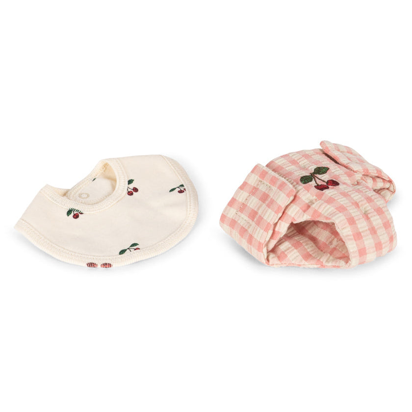 The Konges Slojd Baby Doll Nursery Suitcase features a cream cherry bib and a pink plaid bonnet—ideal accessories for imaginative doll play, displayed flat on a white background.