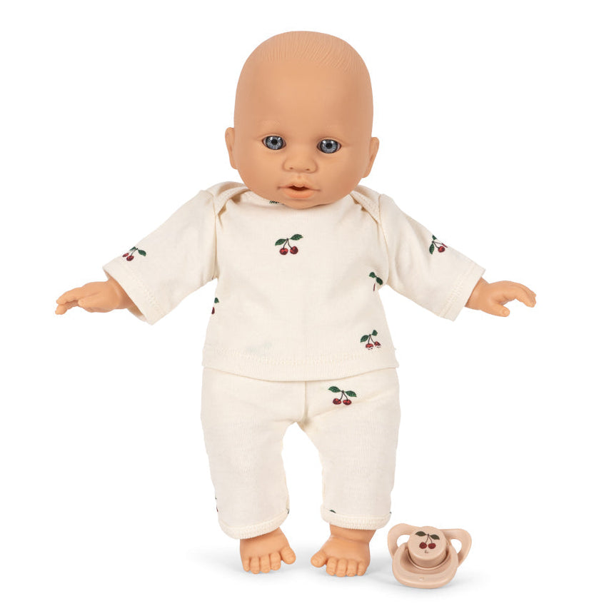 A Poppy Doll Stroller Set doll wearing a cream-colored long-sleeve shirt and cherry-patterned pants, with a matching pacifier on the floor nearby.