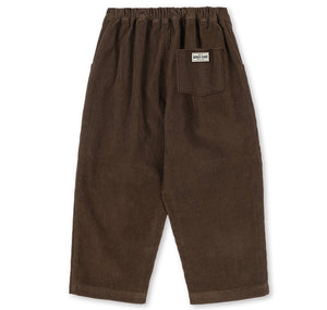 Dark brown relaxed fit Konges Slojd Baby Boys’ and Boys’ Remy Pants with an elastic waistband and a single back pocket featuring a rectangular brand label.