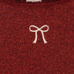 Close-up of a Girls’ Roli Blouse in dark red shimmering glitter with a white embroidered bow and a Konges Slojd brand label at the neckline indicating size 2Y.