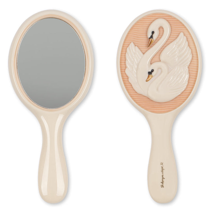 Front and back views of the Konges Slojd Swan Beauty Set hand mirror: one side reflective, the other with a raised swan on peach. Perfect for imaginative play.
