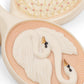 A close-up of the Swan Beauty Set by Konges Slojd, showing a hairbrush adorned with two white swans with black and orange beaks.