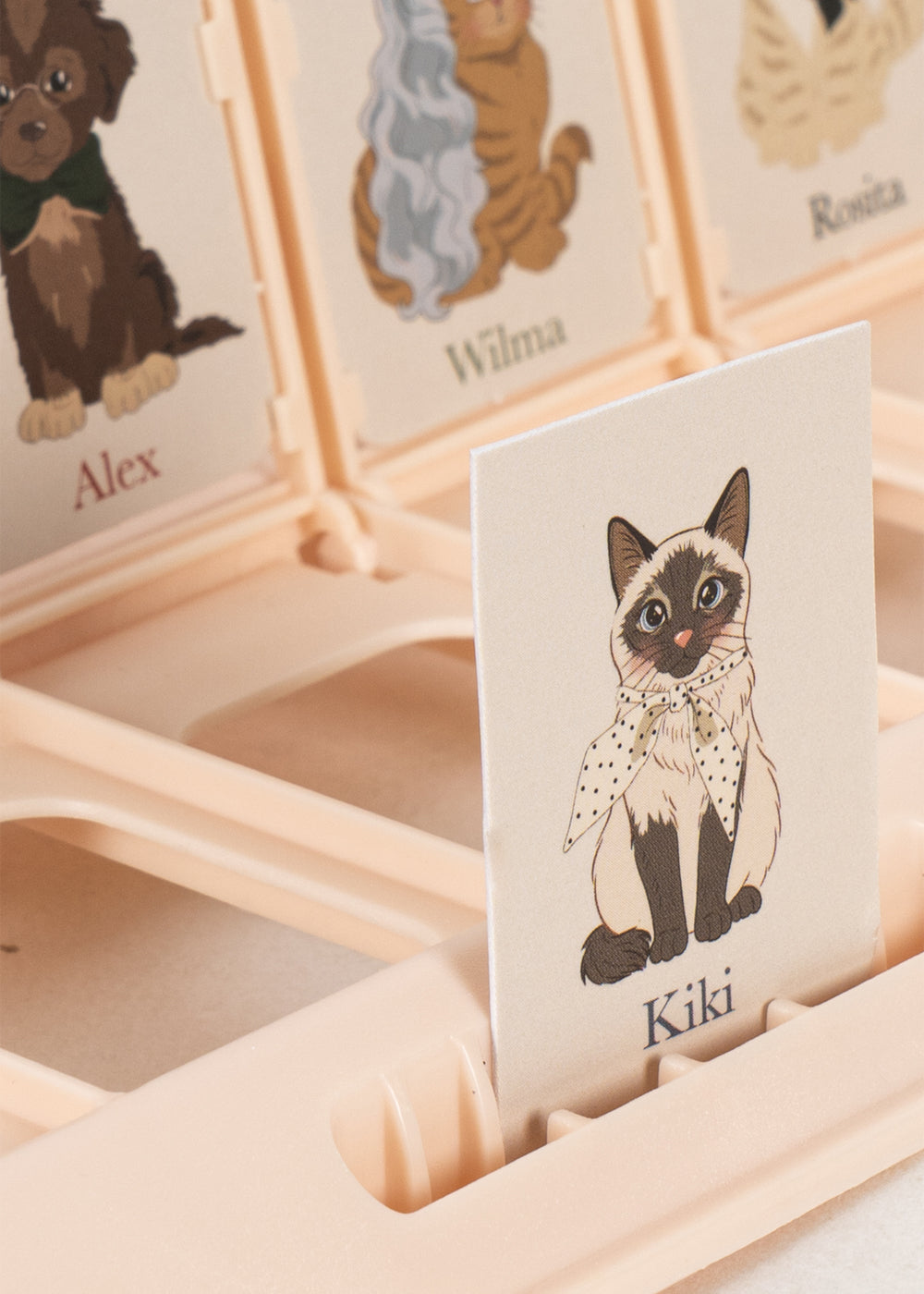 A close-up of the Who Am I Game by Konges Slojd, showing illustrated animal cards and a cat named Kiki in a polka dot scarf.