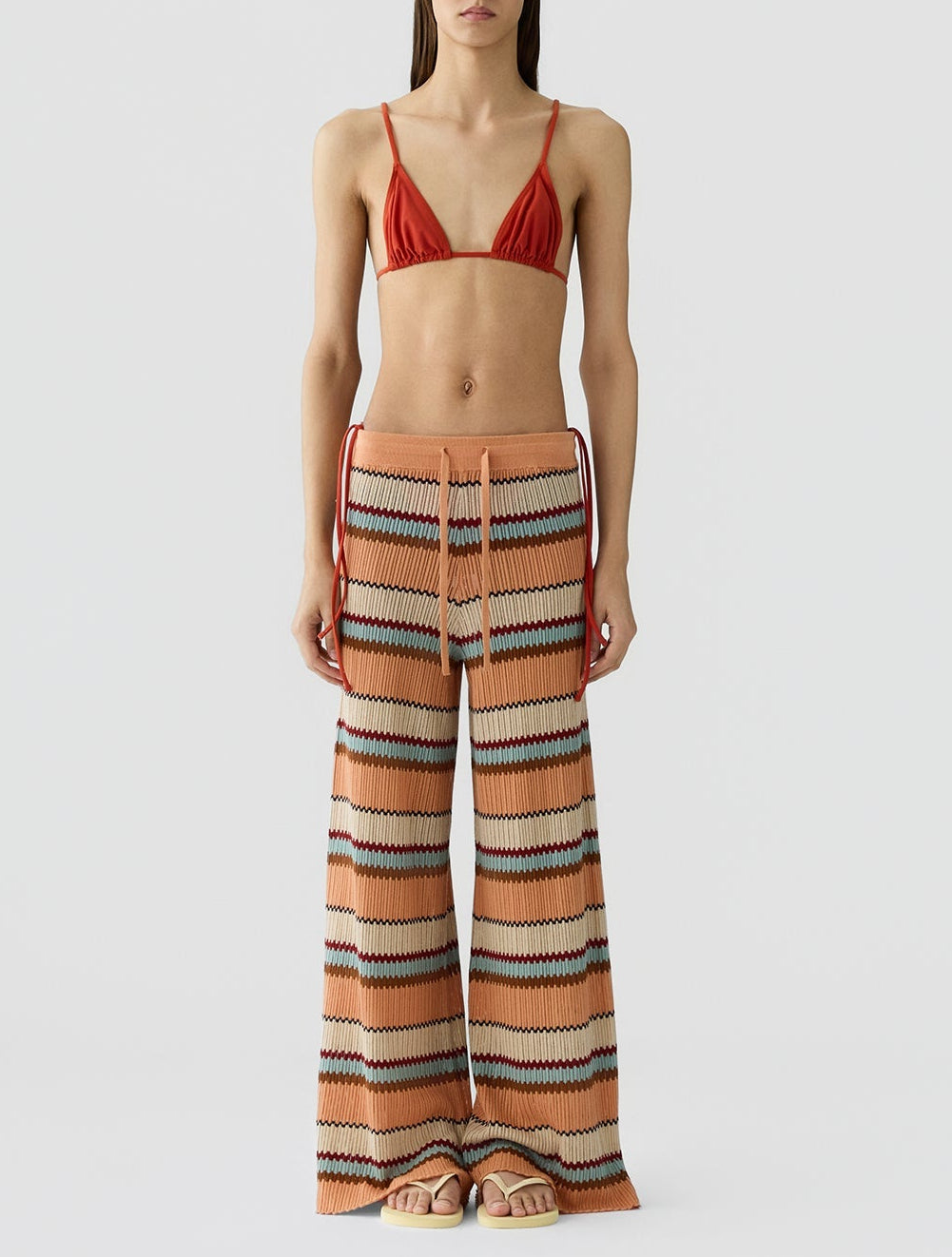 A model wears the Guest in Residence Palazzo Pant featuring a zigzag pattern and wide leg, styled with a rust-colored bikini top, against a plain white background.
