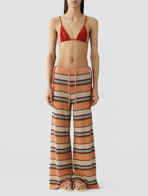 A model wears the Guest in Residence Palazzo Pant featuring a zigzag pattern and wide leg, styled with a rust-colored bikini top, against a plain white background.