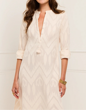 A woman wears the Figue Paolina Kaftan—a cream-colored, patterned, long-sleeve band collar dress with rolled-up sleeves and a partial button-down front—paired with a gold bracelet.