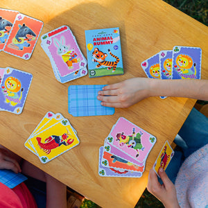 Children eagerly engage in a game of Eeboo Animal Rummy Playing Cards at a wooden table, where the colorful animal-themed cards from the Eeboo brand scatter across the surface. The vintage design of this beloved card game adds an extra layer of charm and nostalgia to their playful afternoon.