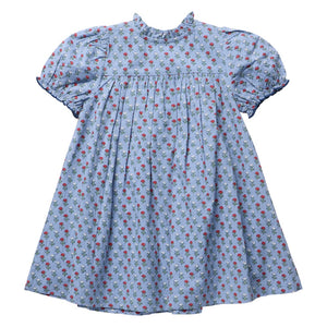 The Girls’ Lucia Dress by Pink Chicken is a light blue short-sleeve dress with a ruffled collar, adorned with a small red and green floral print and detailed delicate navy smocking at the chest and sleeves for added charm.