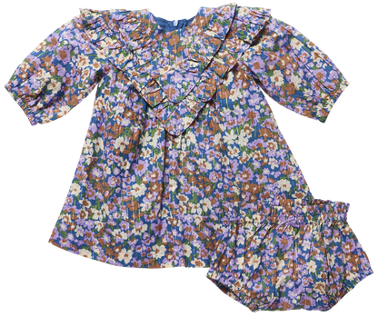 The Baby Girls’ Everly Dress Set by Pink Chicken features a long sleeve floral dress with ruffle collar and matching bloomers in purple, blue, green, and tan prints.
