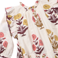 The Girls’ Harper Dress by Pink Chicken features a Harvest Dandelion print, yellow and pink floral embroidery, ruffled shoulders, and a gathered neckline.