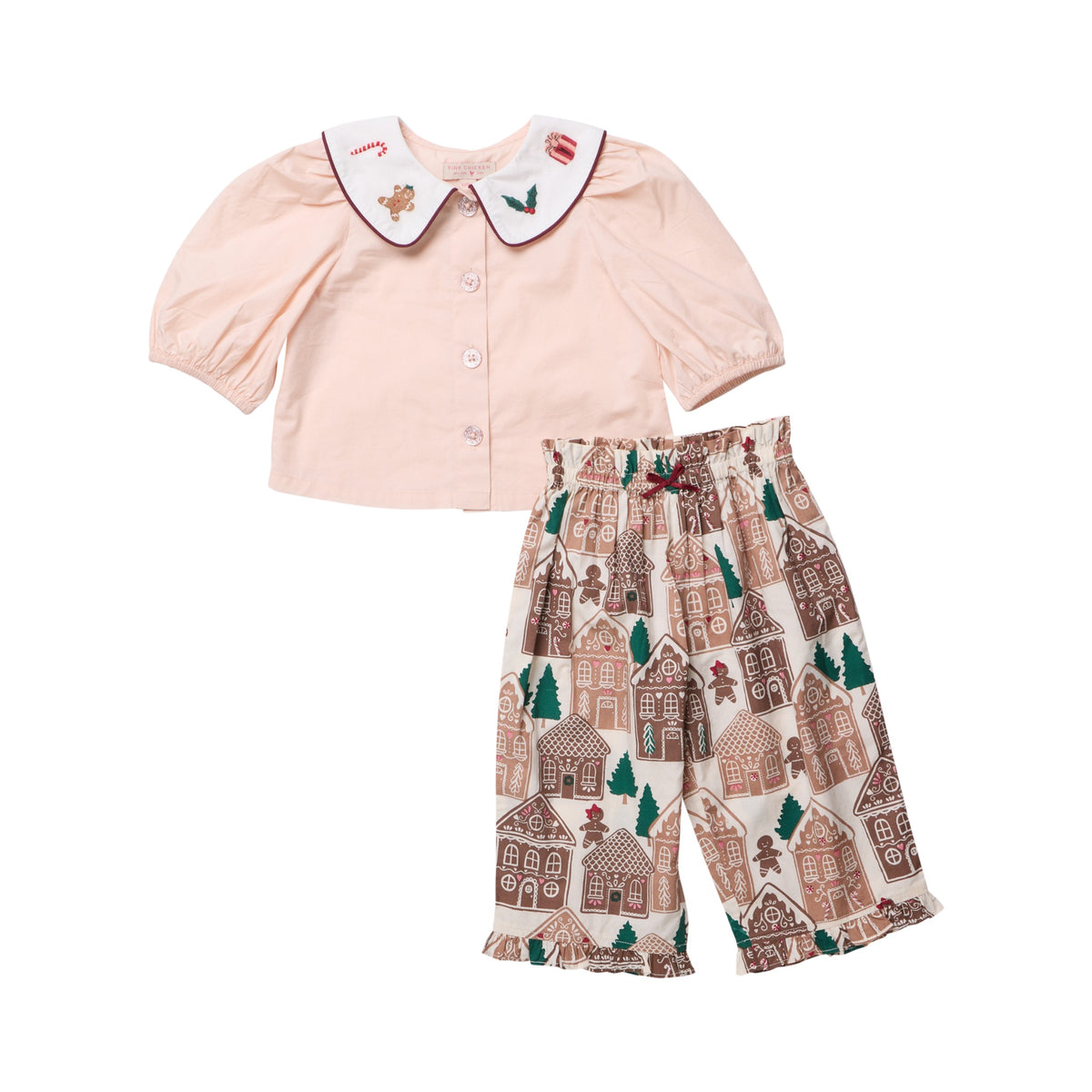 Pink Chicken Baby Girls’ Noelle 2-Piece Set featuring a light pink short-sleeved blouse with a scalloped embroidered collar and cropped pants patterned with gingerbread houses, trees, and cookies.