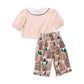 Baby Girls’ Noelle 2-Piece Set featuring a light pink puff-sleeve top with a white collar and cropped pants with a gingerbread house and pine tree print.