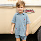 A young child wearing a blue shirt and Pink Chicken Boys’ Calvin Short stands in front of a beige Ford Twin I Beam vehicle.