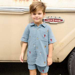 A young child wearing a blue shirt and Pink Chicken Boys’ Calvin Short stands in front of a beige Ford Twin I Beam vehicle.