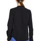 A woman with brown hair in a low ponytail is shown from the back against a white background, wearing the Callas Milano Olympia Top in black with blue pants.