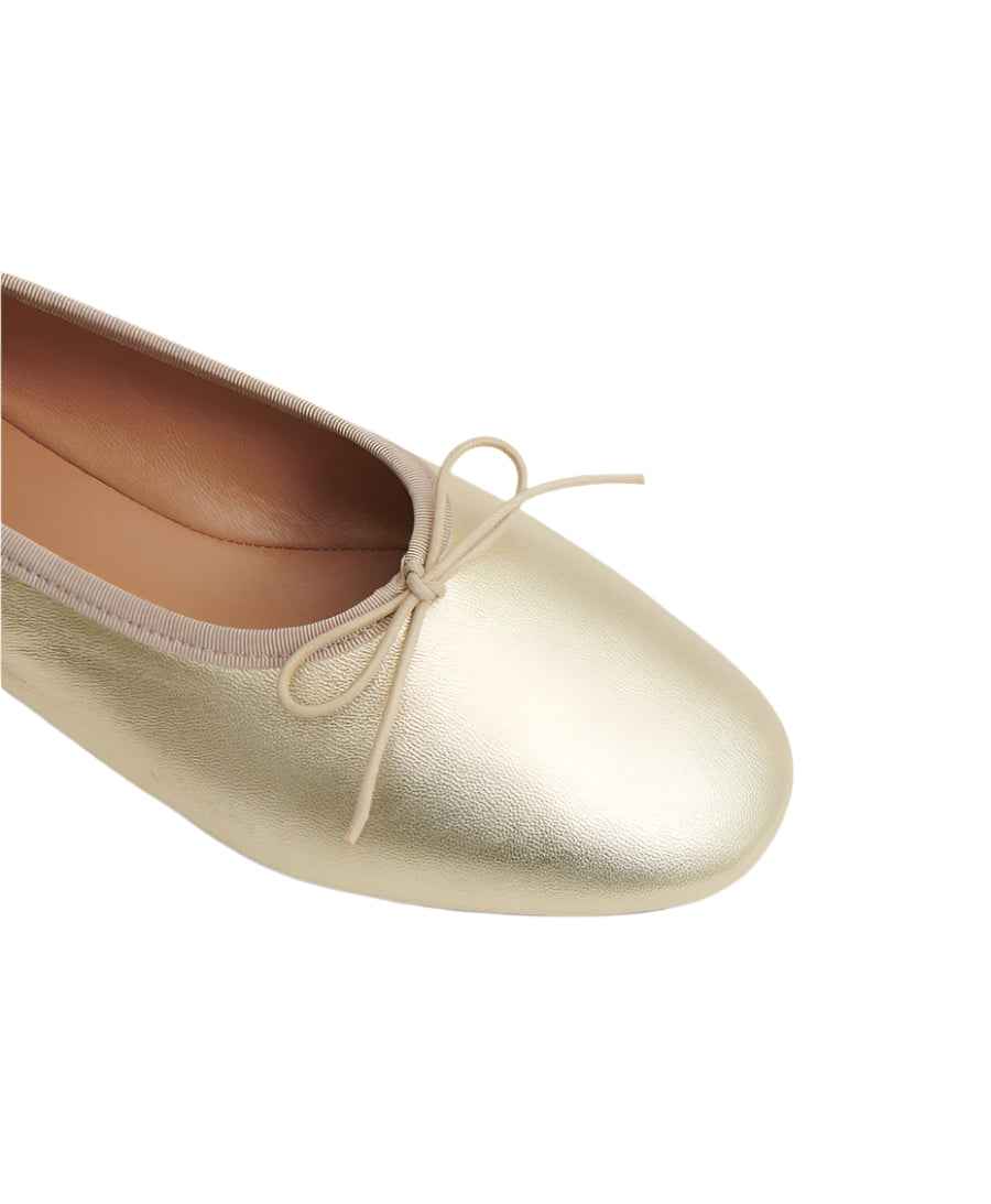 Close-up of Mansur Gavriel's Dream Ballerina, a gold flat made from Italian lambskin leather, featuring a knotted bow on the front and a rounded toe.