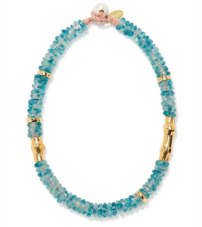 The Toga Beach Necklace by Lizzie Fortunato features cobalt blue recycled glass beads, gold cylindrical accents, a freshwater pearl, and a small gold tag at the clasp.