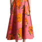 A person is seen from the back wearing the Lela Rose Parker Floral Skirt, a high-waisted cotton poplin style with bold orange floral prints, paired with black low-heeled shoes.