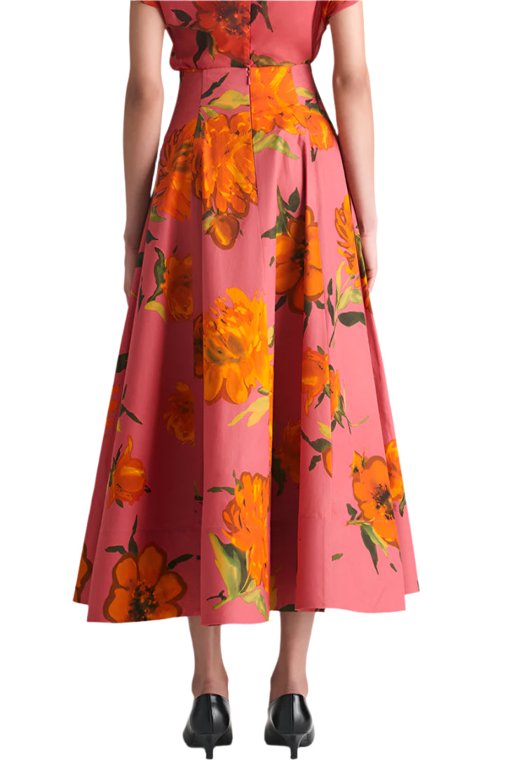 A person is seen from the back wearing the Lela Rose Parker Floral Skirt, a high-waisted cotton poplin style with bold orange floral prints, paired with black low-heeled shoes.