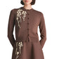 A woman wears the Lela Rose Raffia Embroidered Knit Long Sleeve Cardigan, a brown piece with white floral embroidery on the left side, standing against a white background.