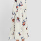 A woman is shown from behind wearing the Erdem Long Sleeve Midi Shirt Dress in white with a rose bouquet print, paired with beige pointed-toe, low-heeled shoes.