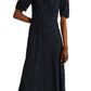 A person wearing the Erdem Short Sleeve Midi Dress, a navy blue, knee-length fit-and-flare style featuring short sleeves and a white floral applique on the left shoulder.