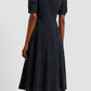 A person stands facing away, wearing the Erdem Short Sleeve Midi Dress in navy jacquard, featuring a knee-length silhouette and a small white detail on the shoulder.