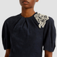 A person wearing the Erdem Short Sleeve Midi Dress—a navy jacquard style with white lace floral applique on one shoulder.