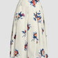 The Erdem Painted Rose Bouquet Pleated Midi Skirt is crafted from white cotton poplin and features a vibrant floral print in blue, red, and pink shades on a light background.