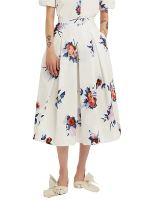Someone dressed in Erdem's Painted Rose Bouquet Pleated Midi Skirt—a white, floral-print, knee-length cotton poplin A-line skirt—paired with a white top and cream bow shoes.