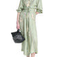 A woman wears the Floyd Dress by Altuzarra—a light green, long-sleeve shirt dress with a point collar, button-down front, abstract print, and wrap tie waist—paired with a black handbag and black flats.