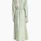 A woman stands with her back to the camera, wearing the Altuzarra Floyd Dress—a light green, long-sleeved shirt dress featuring a classic point collar and a subtle abstract pattern on the back.