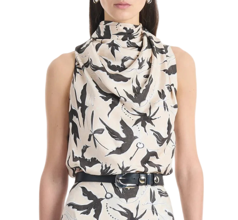 A woman wears the Altuzarra Sleary Top, a sleeveless silk piece with a high cowl neckline and black bird print, paired with a matching high-waisted skirt and black belt.
