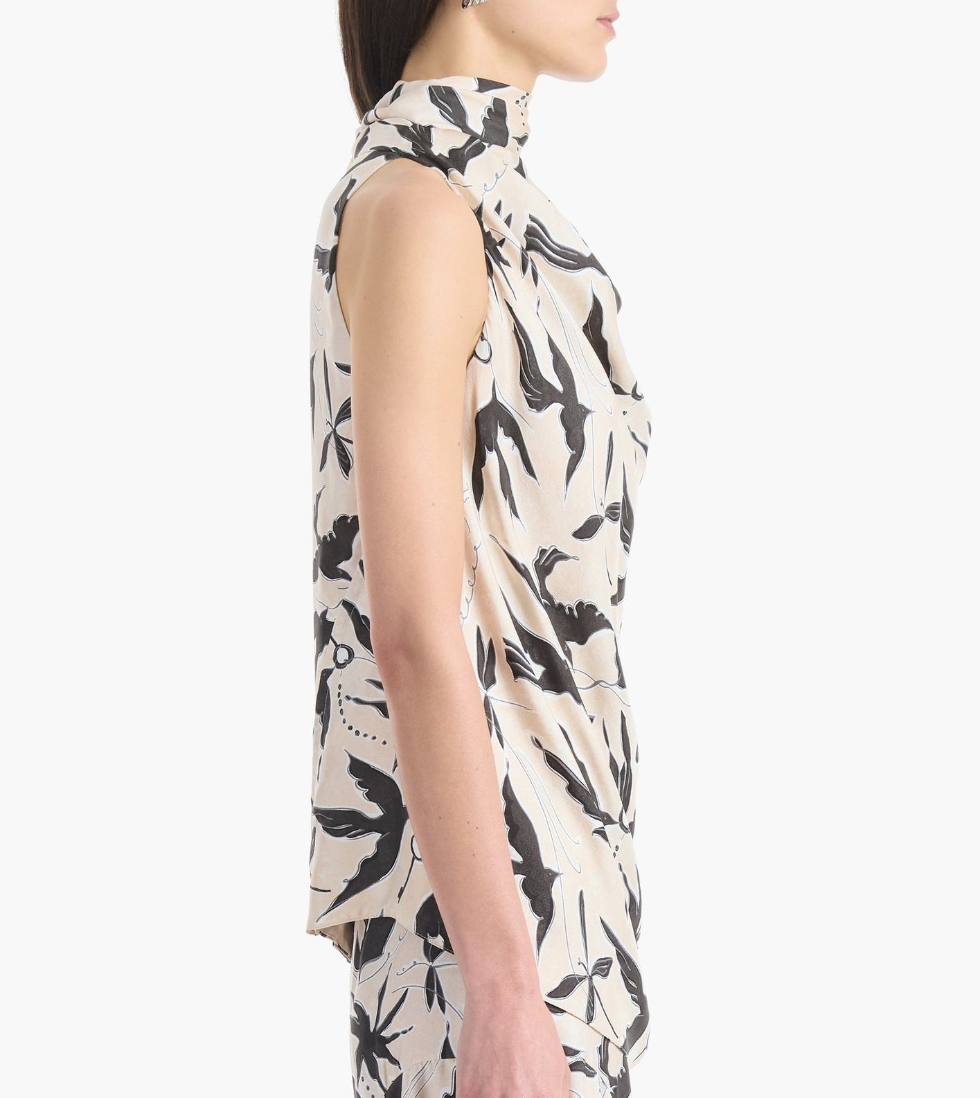 A woman stands in profile wearing the Altuzarra Sleary Top, a sleeveless, high-neck cream silk piece with a black floral print.
